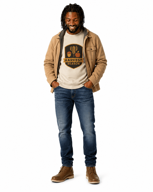 A man modeling a beige jacket over a cream graphic t-shirt, blue jeans, and brown boots against a plain white background.