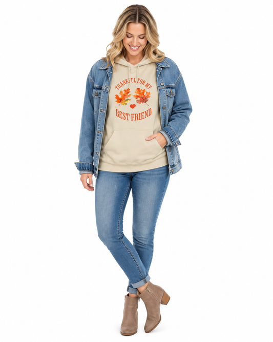 A woman modeling a beige hoodie with an autumn graphic that reads 'THANKFUL FOR MY BEST FRIEND' with orange maple leaves and a small red heart, styled with a blue denim jacket, blue jeans, and taupe ankle boots against a white background.