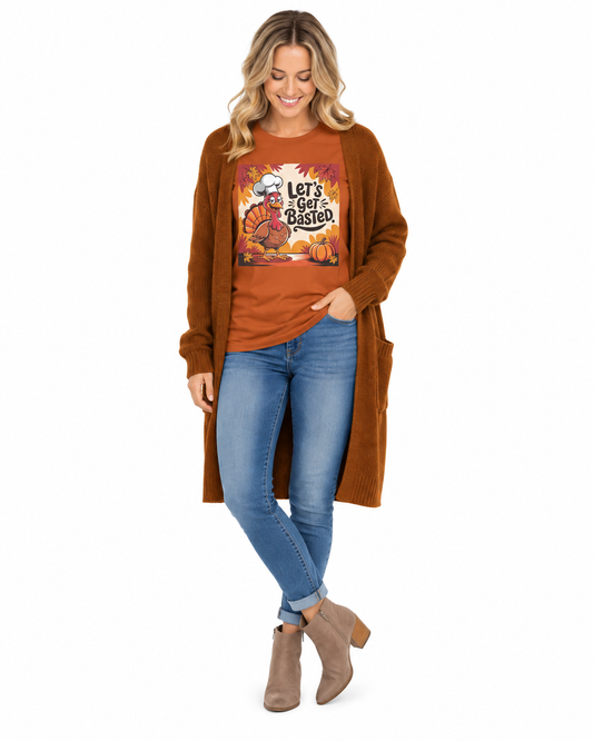 A woman modeling a rust-orange graphic t-shirt with a 'Let's Get Bashed' autumn design, layered under a long brown cardigan, paired with blue jeans and taupe ankle boots, on a white background.