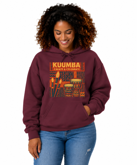 A woman with curly brown hair wearing a maroon hoodie with a colorful 'KUUMBA CREATE & CELEBRATE' graphic on the chest, paired with blue jeans, against a plain white background.