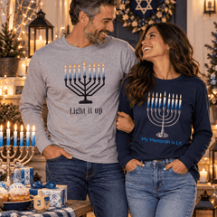 Couple wearing Hanukkah long sleeve shirts in a festive outdoor setting with menorah and holiday lights