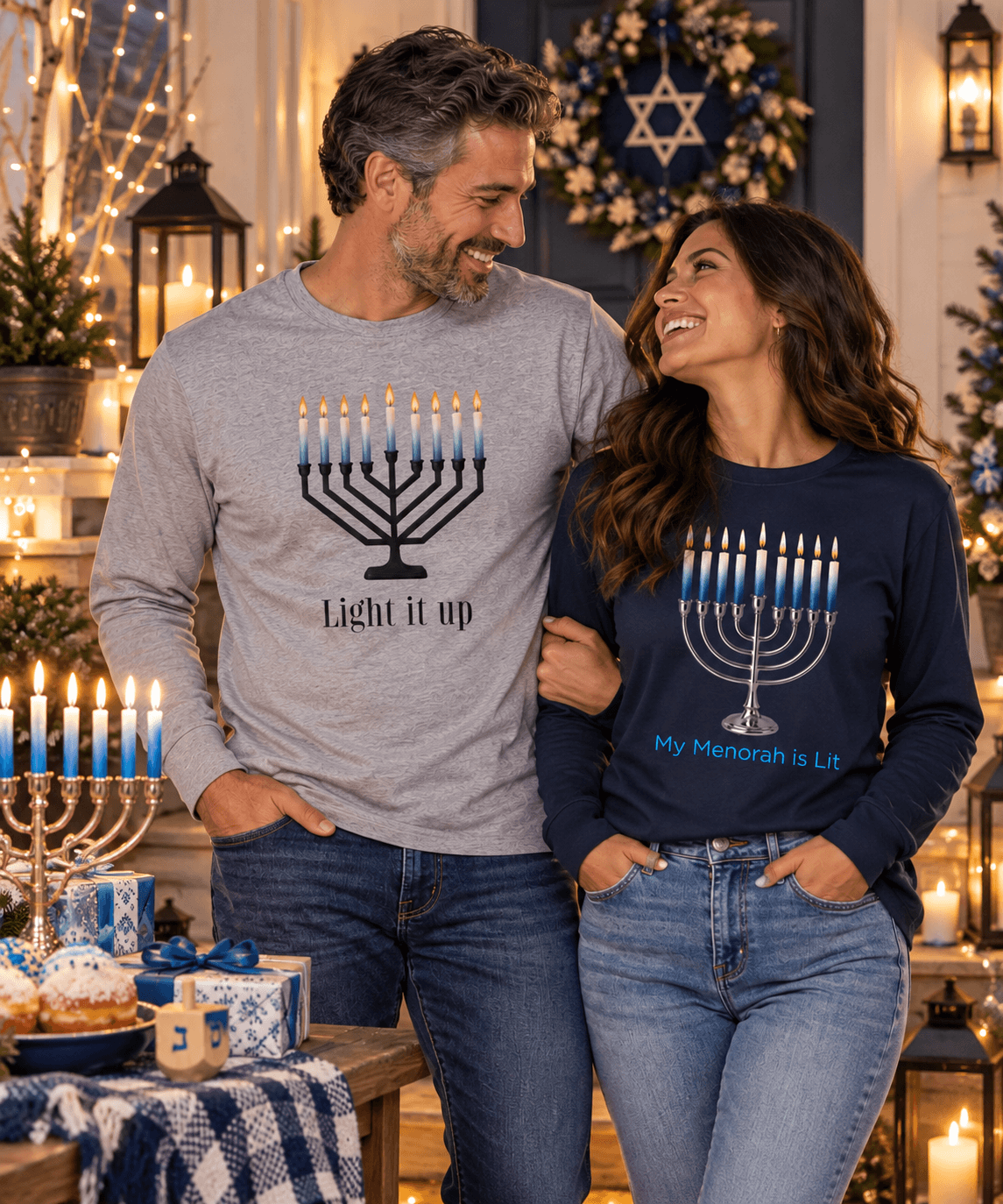 Couple wearing Hanukkah long sleeve shirts in a festive outdoor setting with menorah and holiday lights