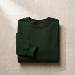 Folded forest green sweatshirt displayed on textured linen fabric.