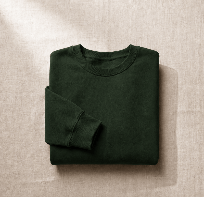 Folded forest green sweatshirt displayed on textured linen fabric.