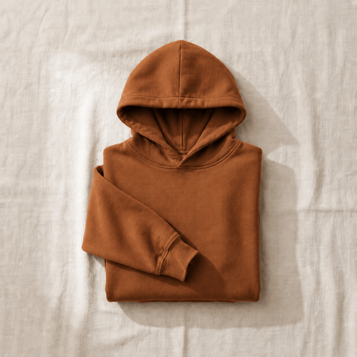 Folded autumn color hoodie on neutral linen background.