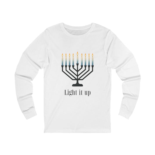 A white long-sleeve t-shirt with a graphic of a black menorah with blue-to-yellow lit candles and the text 'Light it up' printed below, displayed on a clean white background.