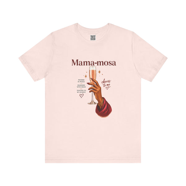 A light pink short-sleeve t-shirt with a graphic print on the front. The print features the text 'Mama-mosa' in a dark reddish-brown font, an illustration of a hand holding a champagne flute, and decorative text elements.