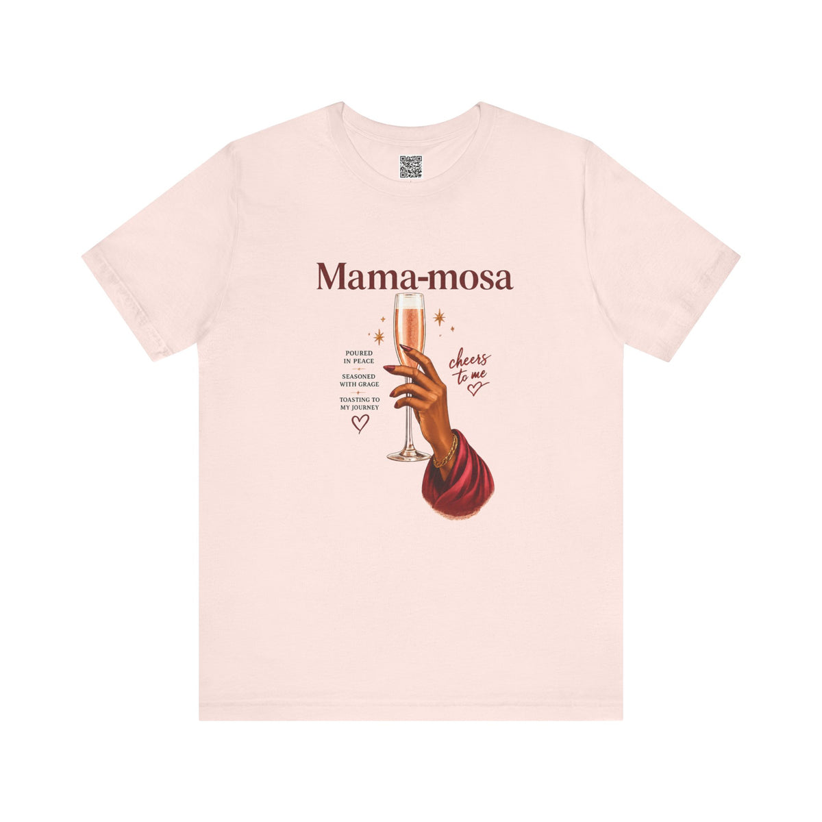 A light pink short-sleeve t-shirt with a graphic print on the front. The print features the text 'Mama-mosa' in a dark reddish-brown font, an illustration of a hand holding a champagne flute, and decorative text elements.