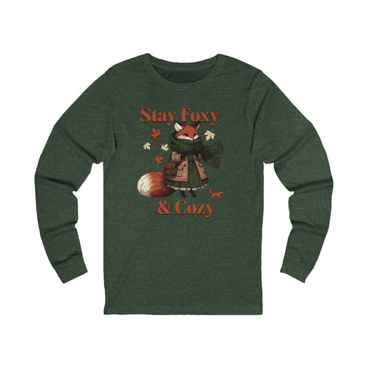 A dark heather green long-sleeve t-shirt featuring a graphic of a cozy fox wearing a green scarf and brown coat, surrounded by autumn leaves, with the text 'Stay Foxy & Cozy' in orange.