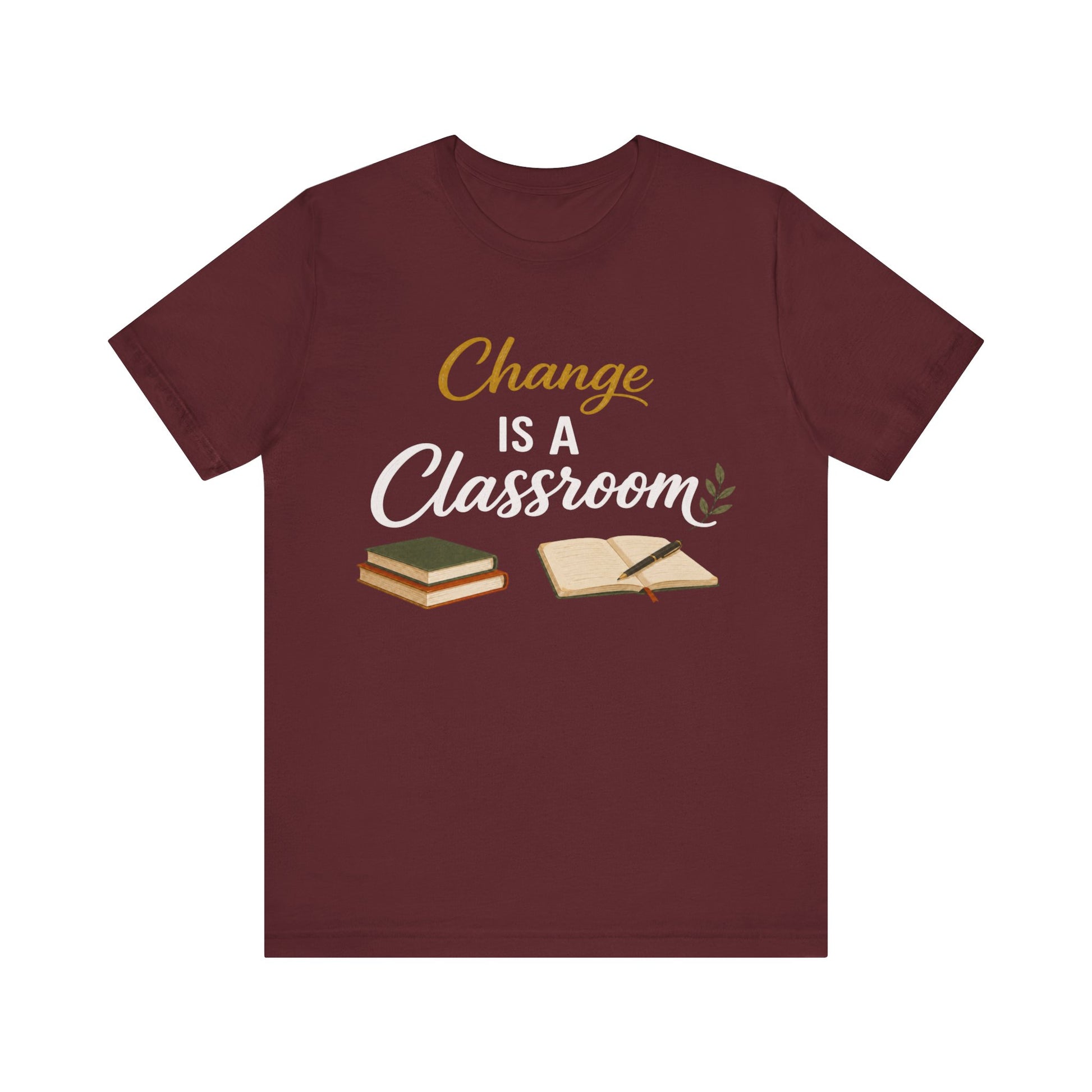A maroon short-sleeve crewneck t-shirt with a graphic on the chest that reads 'Change IS A Classroom' in white and gold lettering, accompanied by illustrations of stacked books and an open notebook, displayed on a solid white background.