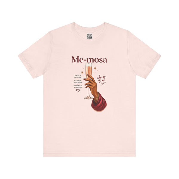 A light pink short-sleeve crewneck t-shirt featuring a graphic print of a hand holding a champagne flute with the text 'Me-mosa' and 'cheers to me' on a solid white background.