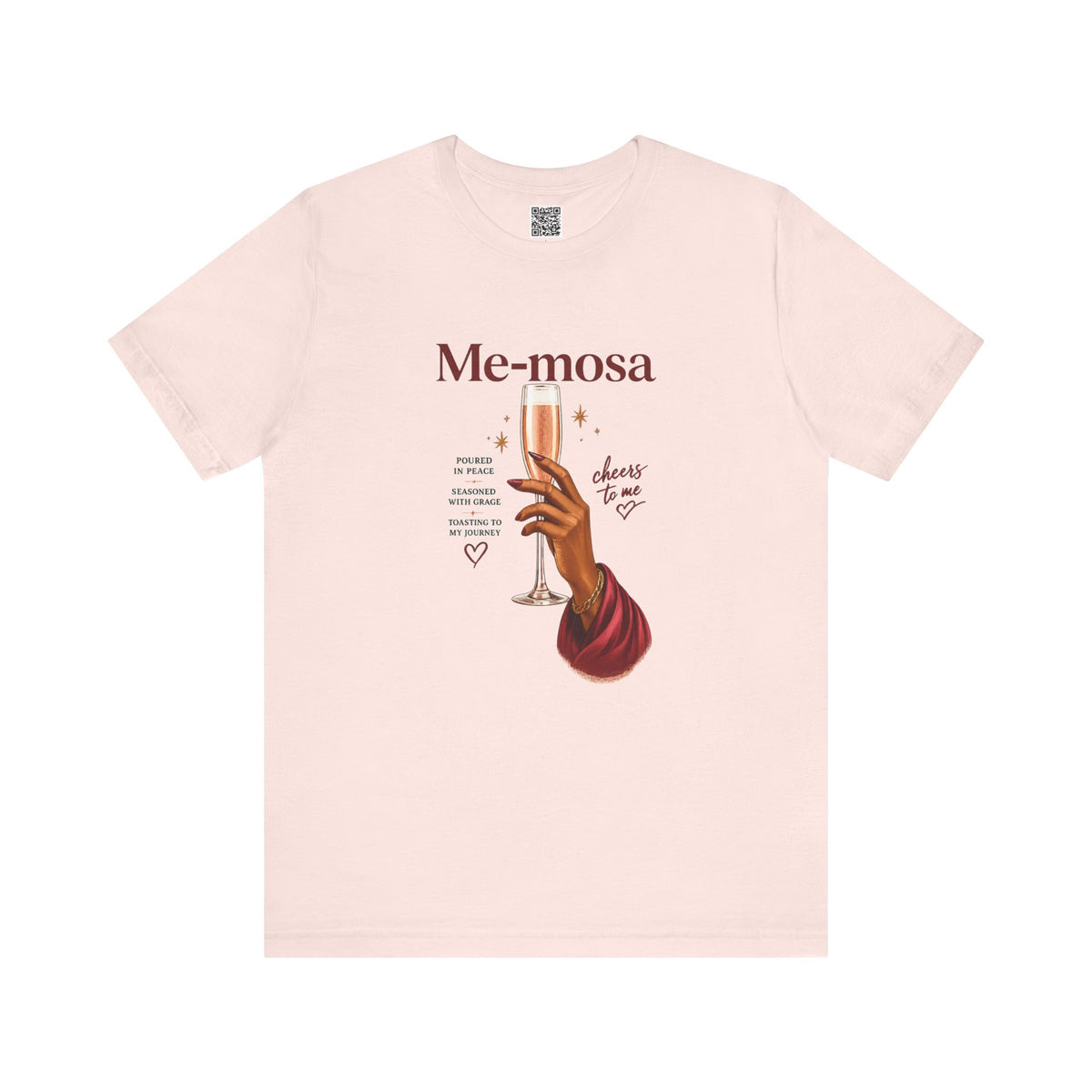 A light pink short-sleeve crewneck t-shirt featuring a graphic print of a hand holding a champagne flute with the text 'Me-mosa' and 'cheers to me' on a solid white background.