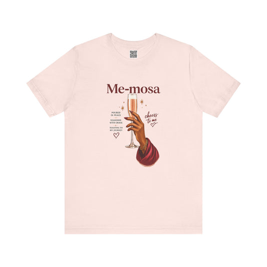 A light pink short-sleeve crewneck t-shirt featuring a graphic print of a hand holding a champagne flute with the text 'Me-mosa' and 'cheers to me' on a solid white background.