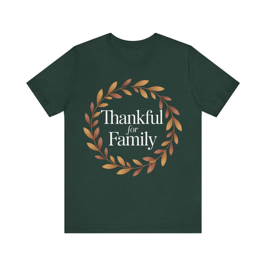 A dark forest green short-sleeve t-shirt with a graphic on the chest featuring a circular wreath of brown and orange leaves surrounding the white serif text 'Thankful for Family'.