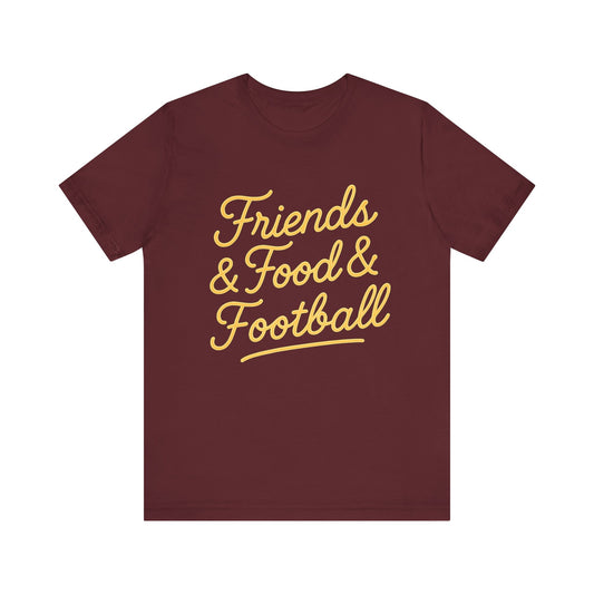 A maroon short-sleeve crewneck t-shirt with 'Friends & Food & Football' printed in yellow cursive text across the chest, displayed on a solid white background.