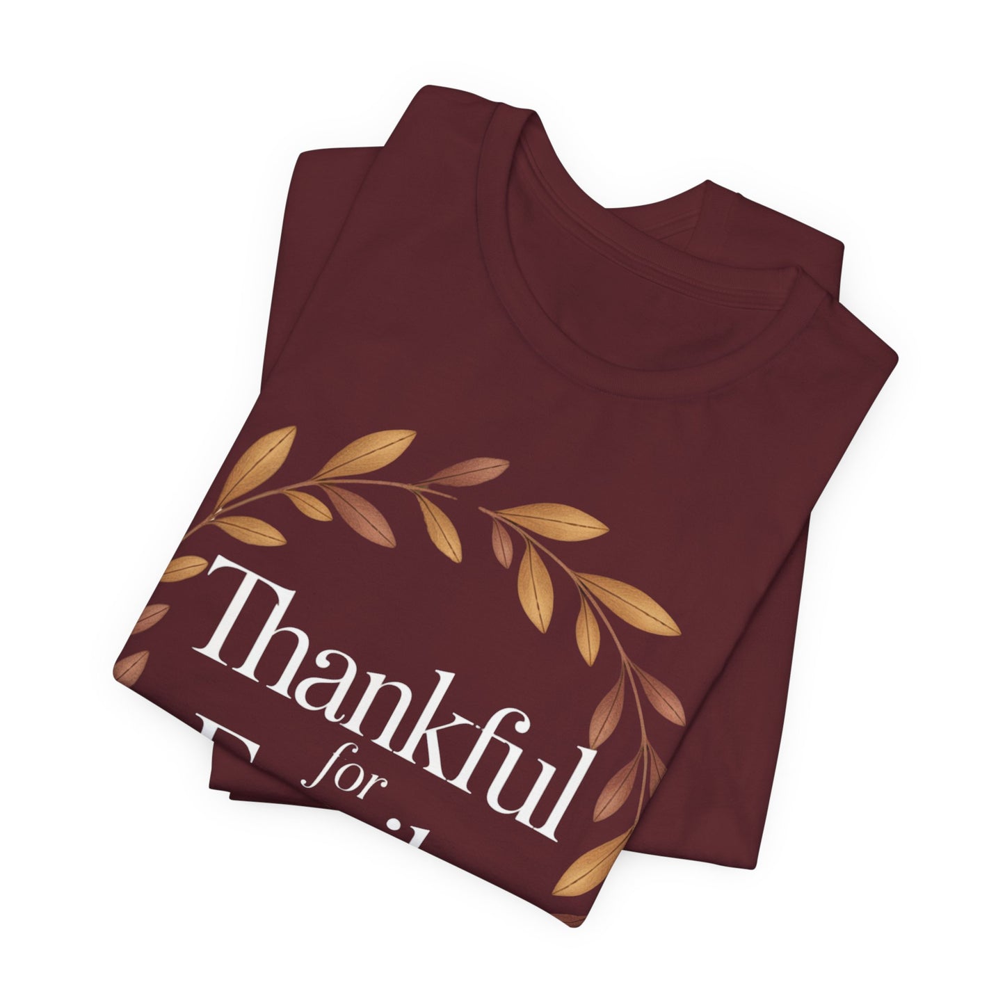 A folded maroon t-shirt with a graphic print featuring a gold leaf wreath and the text 'Thankful for' in white, displayed on a clean white background.