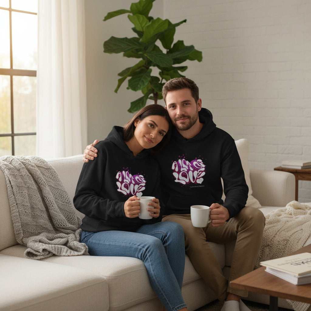 Two people sitting on a couch wearing matching black hoodies with colorful designs, holding coffee mugs.