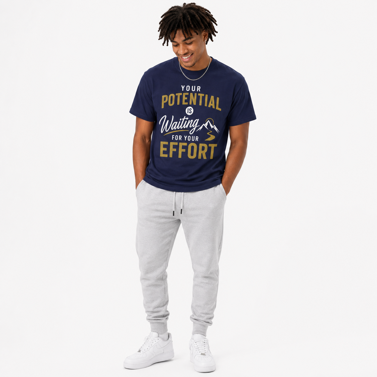 A man wearing a navy blue graphic t-shirt with gold and white text, paired with light gray sweatpants and white sneakers, standing against a plain white background.