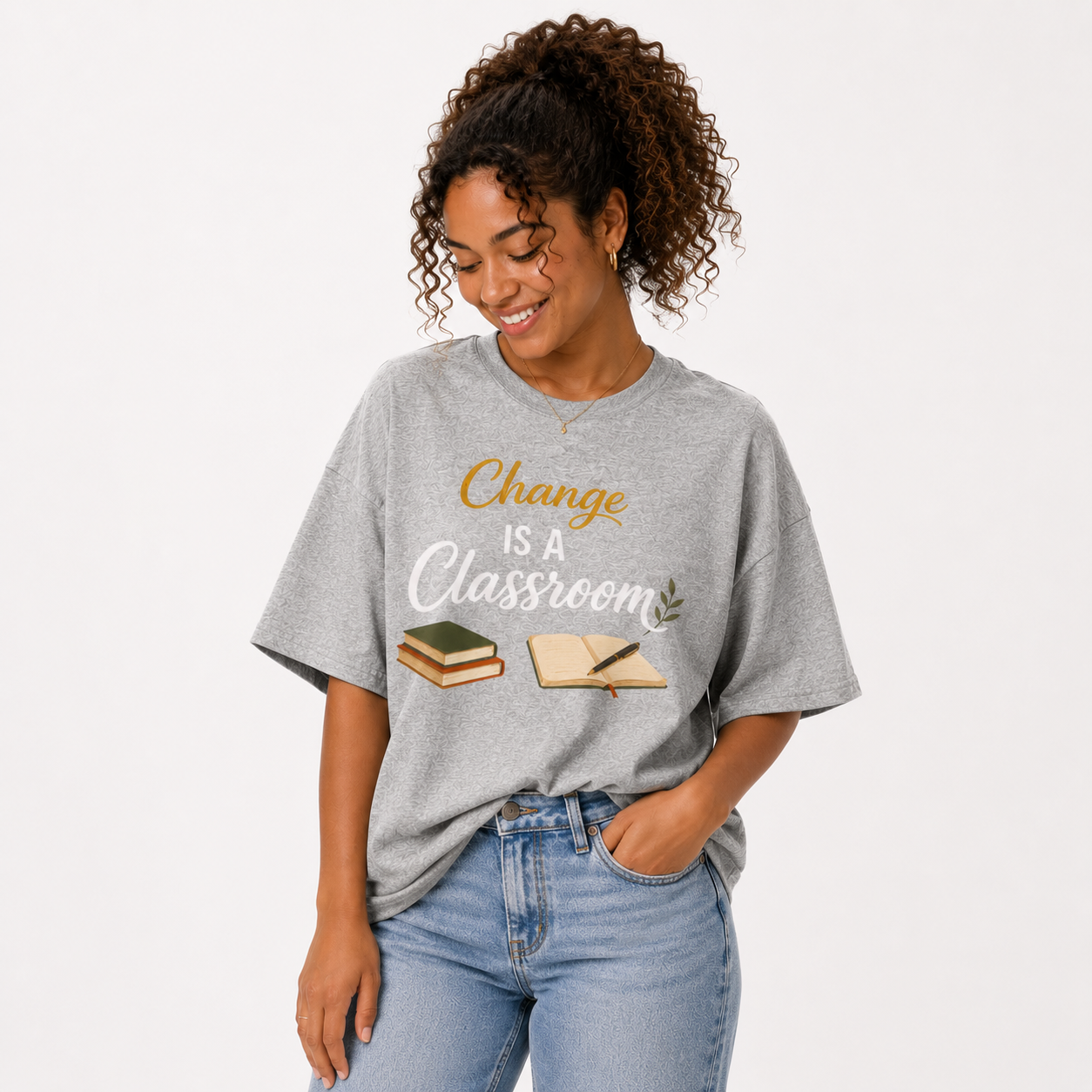 A woman wearing a heather gray graphic t-shirt with the text 'Change IS A Classroom' in gold and white, paired with light blue jeans, against a plain white background.