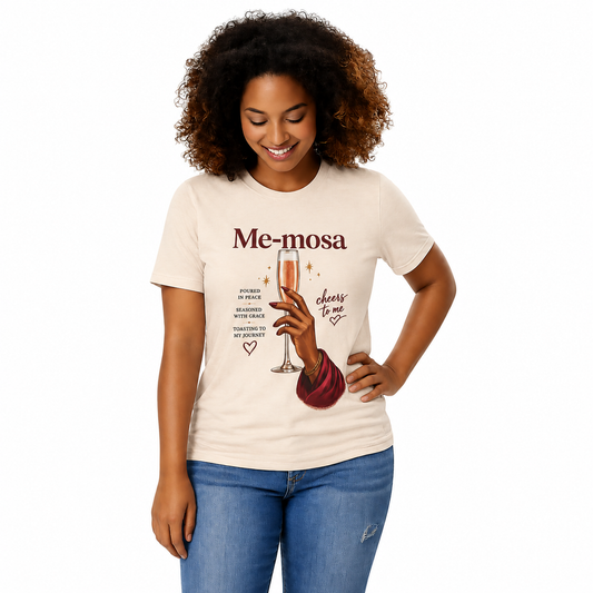 A woman wearing a cream-colored graphic t-shirt with the text 'Me-mosa' and an illustration of a hand holding a champagne glass, paired with blue jeans, against a plain white background.