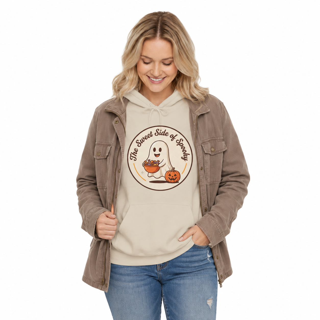 A woman modeling a beige hoodie with a 'The Sweetest Side of Halloween' ghost and pumpkin graphic, layered under a brown corduroy jacket, paired with blue jeans, on a white background.