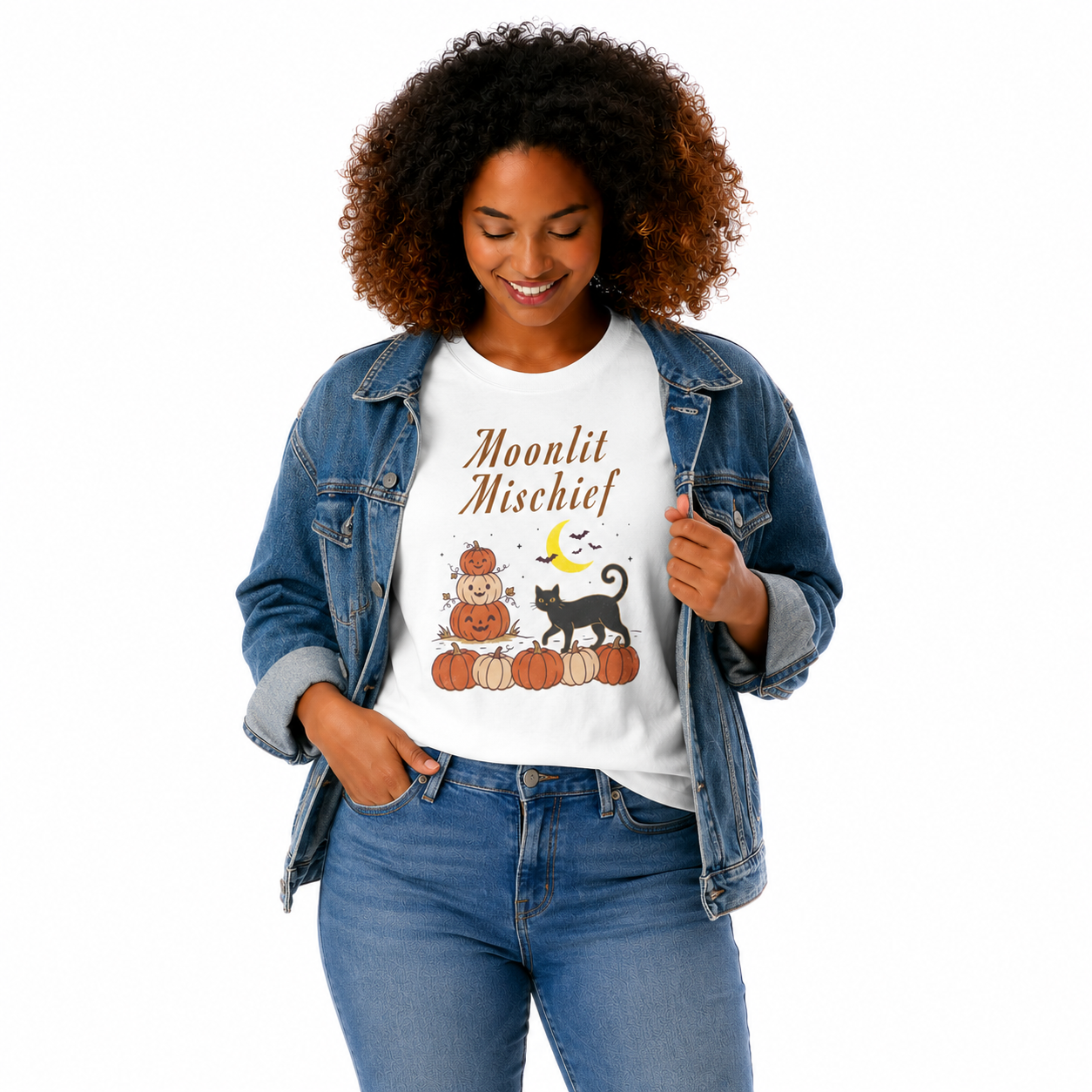 A woman wearing a white graphic t-shirt with a 'Moonlit Mischief' autumn pumpkin and cat design, styled with a blue denim jacket and blue jeans against a plain white background.