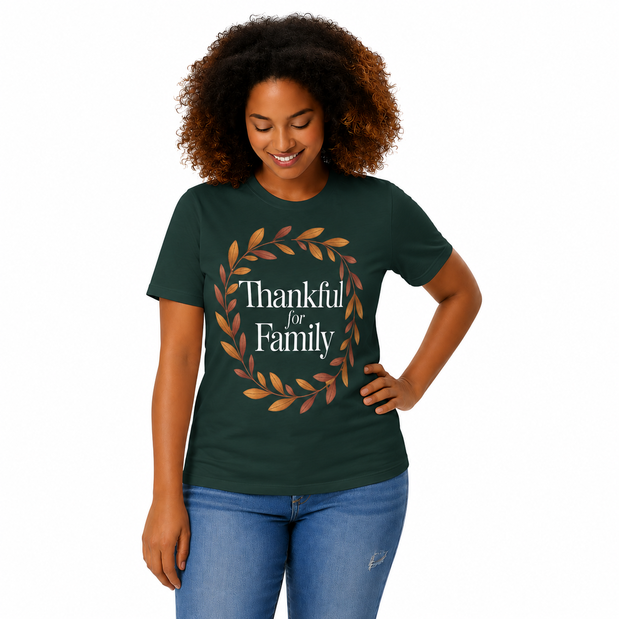 A woman with curly brown hair wearing a dark green t-shirt with a 'Thankful for Family' graphic in white text and a brown and orange leaf wreath, paired with blue jeans, against a plain white background.