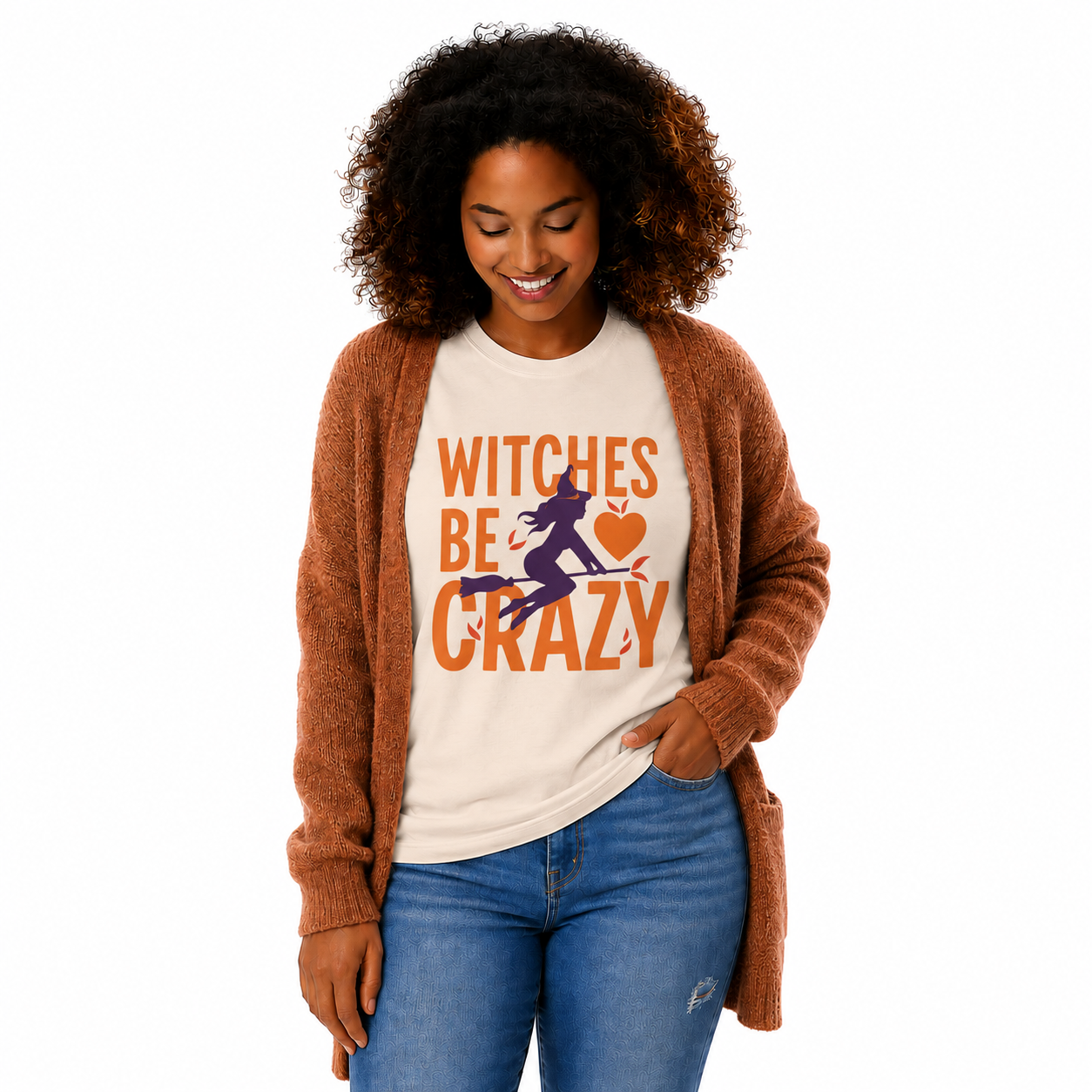 A woman wearing a cream graphic t-shirt with the text 'WITCHES BE CRAZY' and a witch riding a broomstick, styled with a brown cardigan and blue jeans against a white background.