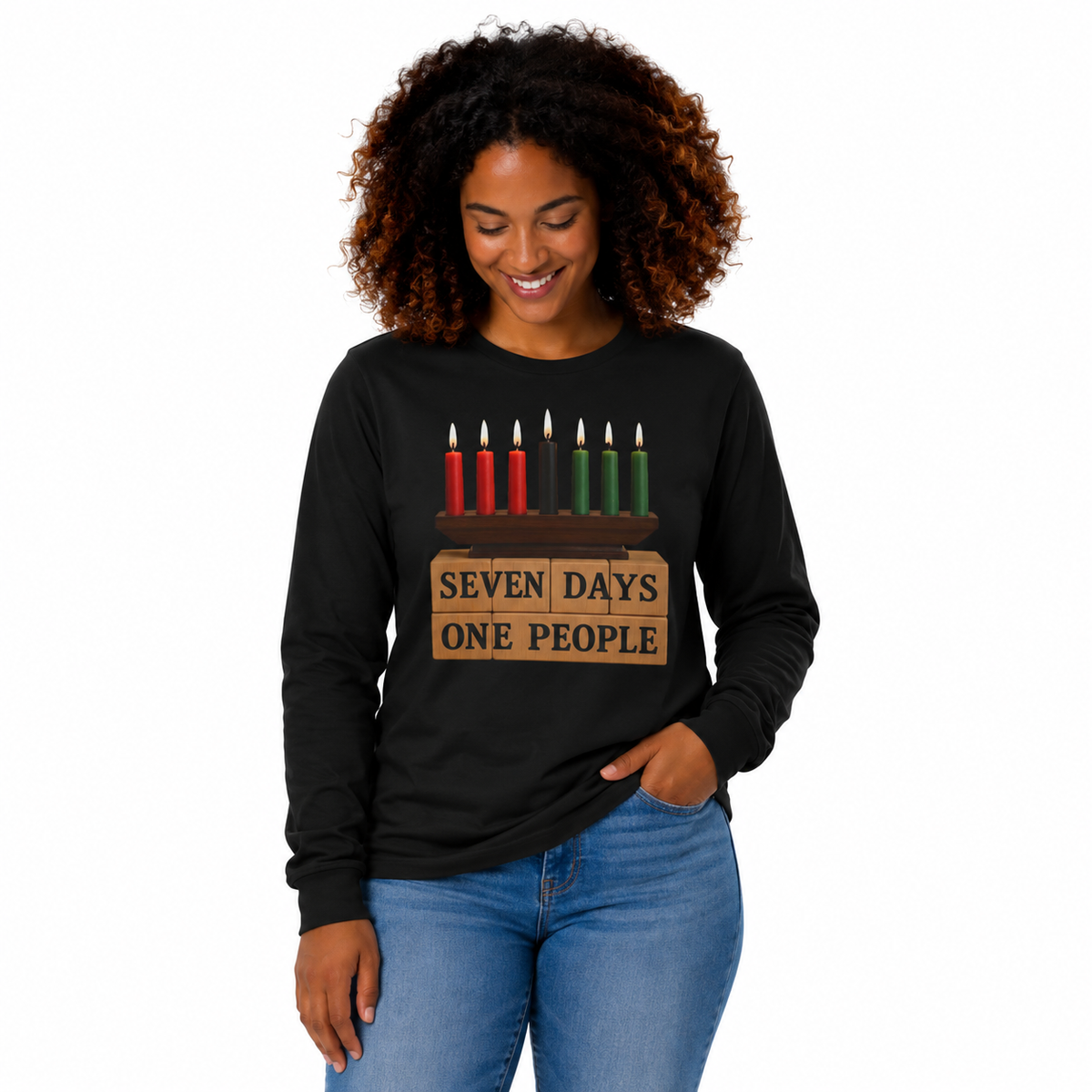 A woman with curly brown hair wearing a black long-sleeve t-shirt with a graphic of a seven-day candle menorah and the text 'SEVEN DAYS ONE PEOPLE', paired with blue jeans, against a plain white background.