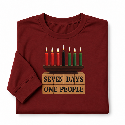 A folded maroon crewneck t-shirt with a graphic of a menorah on top of wooden blocks that read 'SEVEN DAYS ONE PEOPLE'. The graphic features red, black, and green candles, and the t-shirt is displayed on a clean white background.