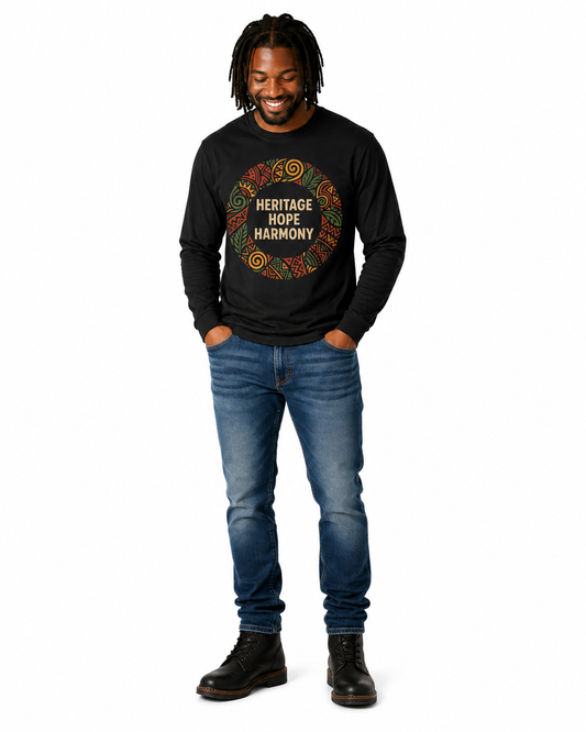 A man wearing a black long-sleeve t-shirt with a colorful circular graphic that reads 'HERITAGE HOPE HARMONY', paired with blue jeans and black boots, standing against a plain white background.