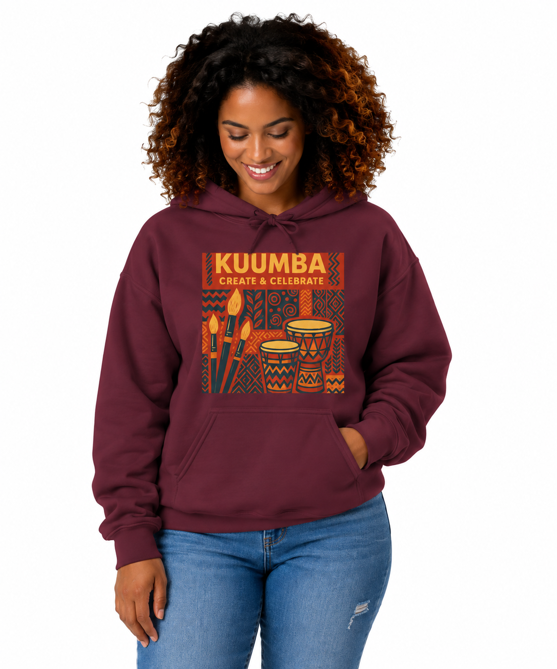 A woman with curly brown hair wearing a maroon hoodie with a colorful 'KUUMBA CREATE & CELEBRATE' graphic on the chest, paired with blue jeans, against a plain white background.