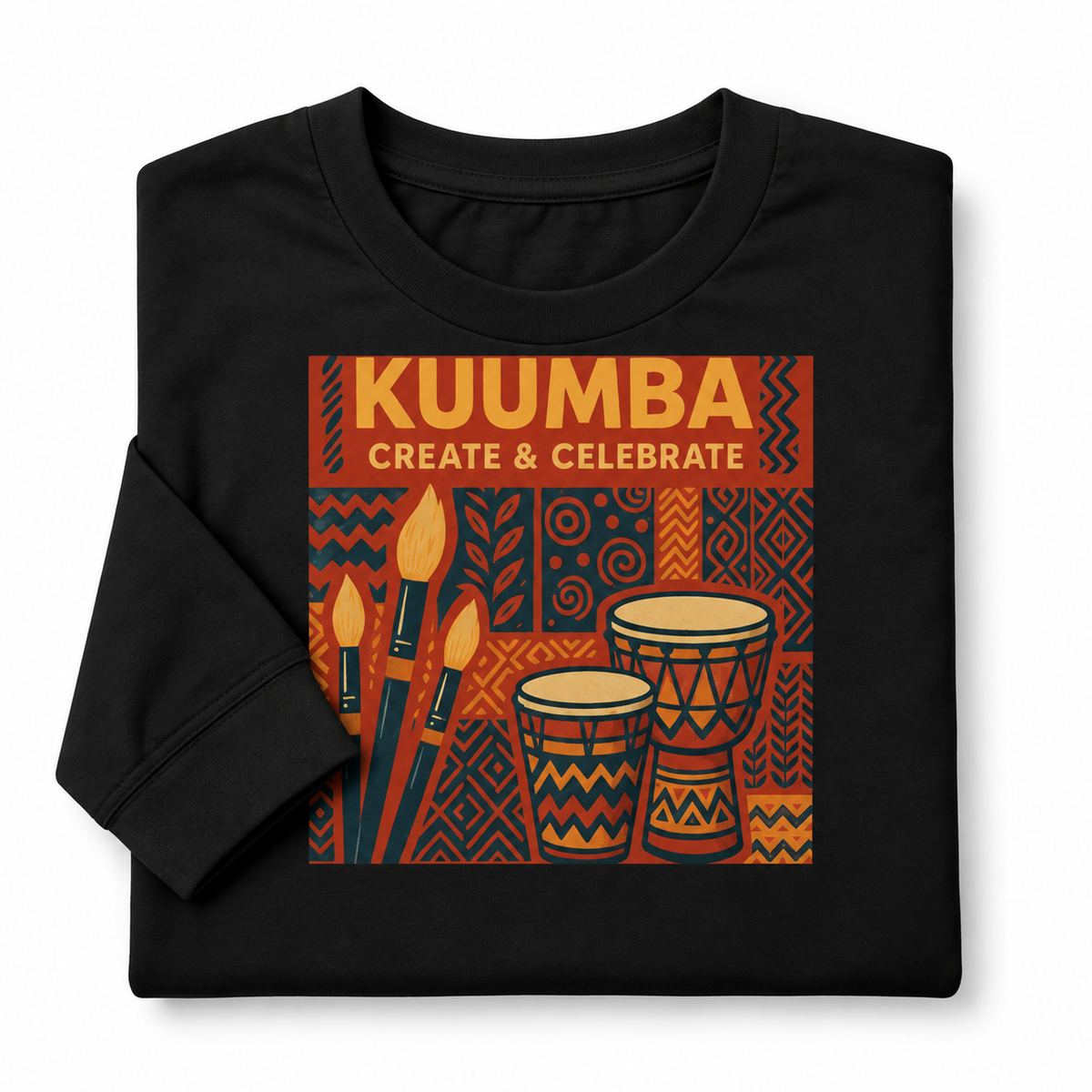 A folded black t-shirt with a colorful graphic print featuring the text 'KUUMBA CREATE & CELEBRATE' above illustrations of paintbrushes and djembe drums on a patterned orange and black background.