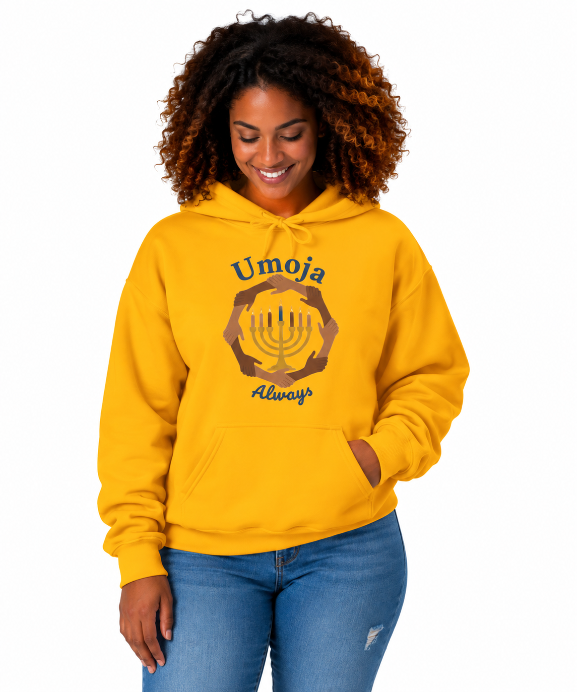 A woman with curly brown hair wearing a bright yellow hoodie with a 'Umoja Always' graphic featuring a menorah and hands, paired with blue jeans, against a plain white background.