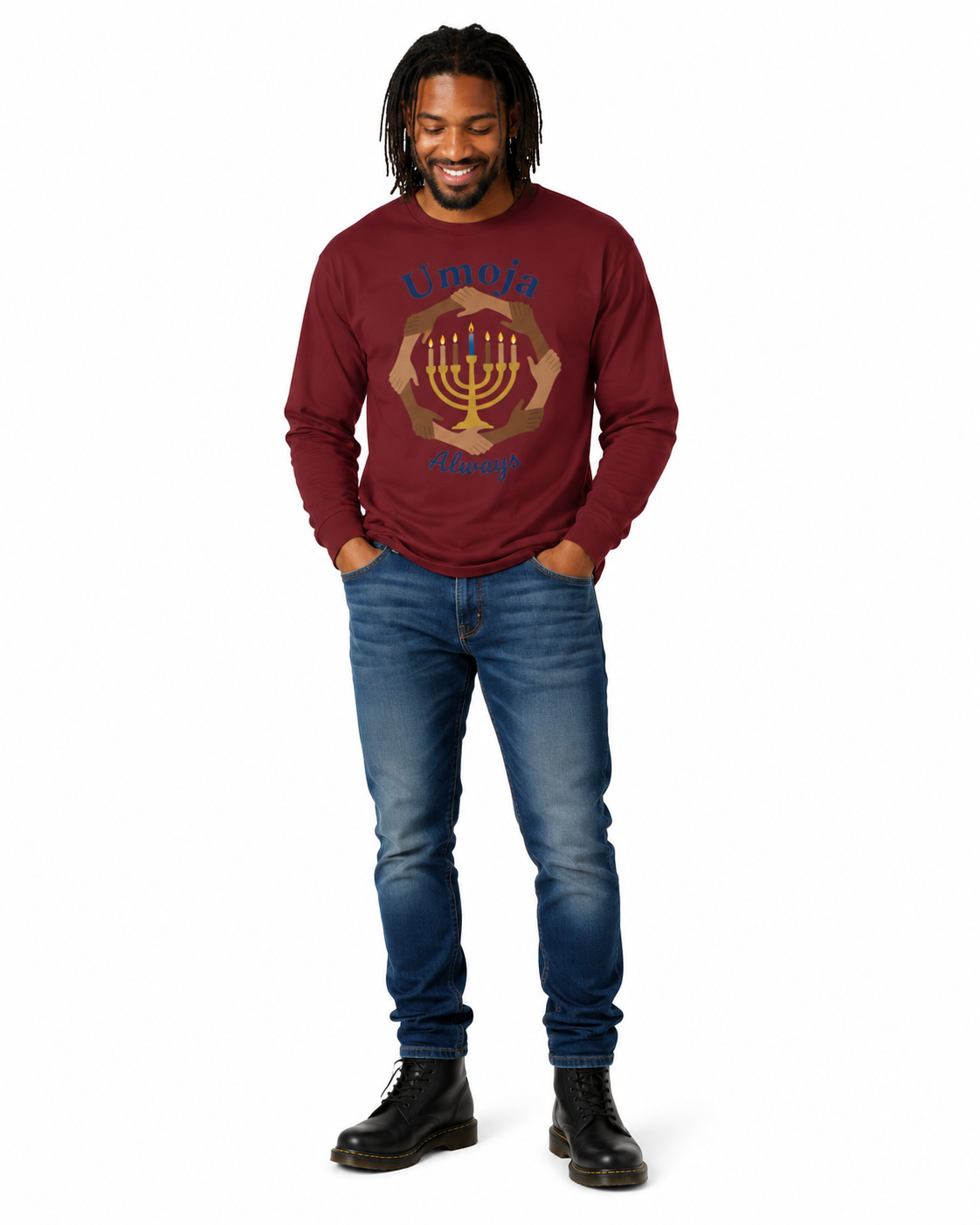 A man wearing a maroon long-sleeve shirt with a gold and blue Menorah graphic and the words 'Umoja Always' on the front, paired with blue jeans and black boots, standing against a white background.