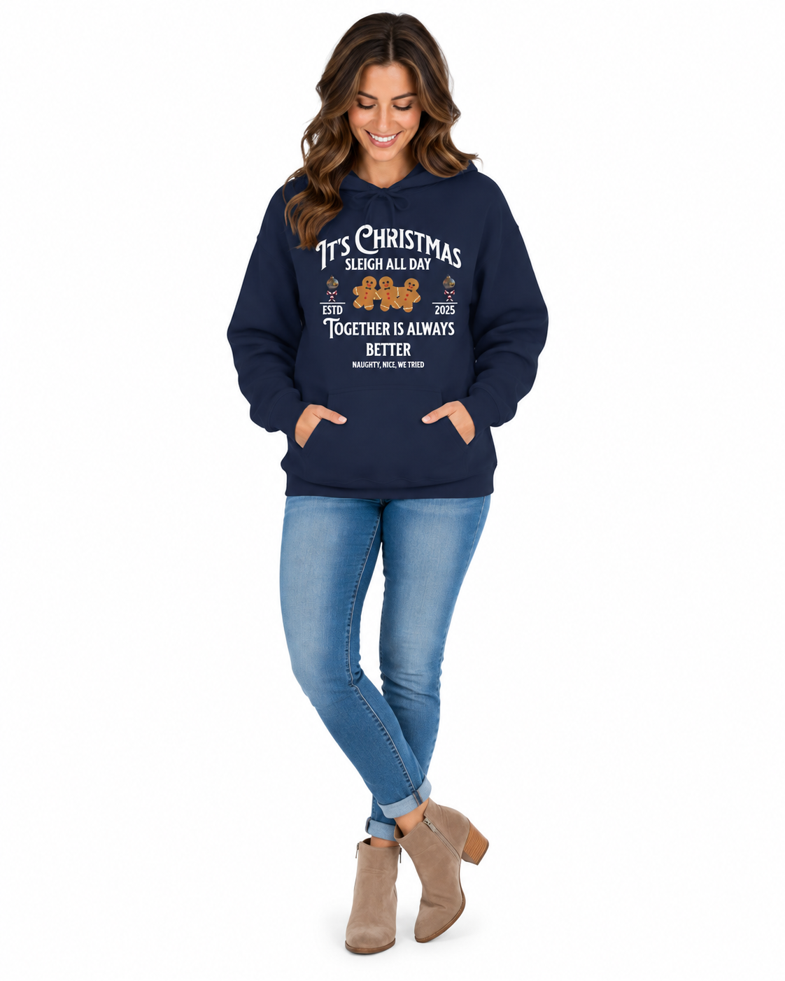 A woman modeling a navy blue hoodie with a Christmas-themed graphic print that reads 'It's Christmas Sleigh All Day Together is Always Better' with a small train illustration. She is wearing blue jeans and beige ankle boots against a plain white background.