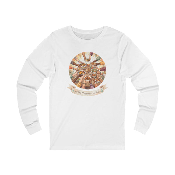 A white long-sleeve crewneck t-shirt featuring a circular graphic on the chest depicting a multi-colored Passover Seder table with hands reaching toward food, and a banner below reading 'All Are Welcome at My Table'.