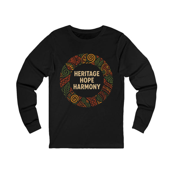 A black long-sleeve t-shirt with a circular graphic on the chest featuring the words 'HERITAGE HOPE HARMONY' in beige, surrounded by a pattern of orange, green, and brown tribal-style designs, shown on a plain white background.