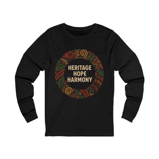 A black long-sleeve t-shirt with a circular graphic on the chest featuring the words 'HERITAGE HOPE HARMONY' in beige, surrounded by a pattern of orange, green, and brown tribal-style designs, shown on a plain white background.