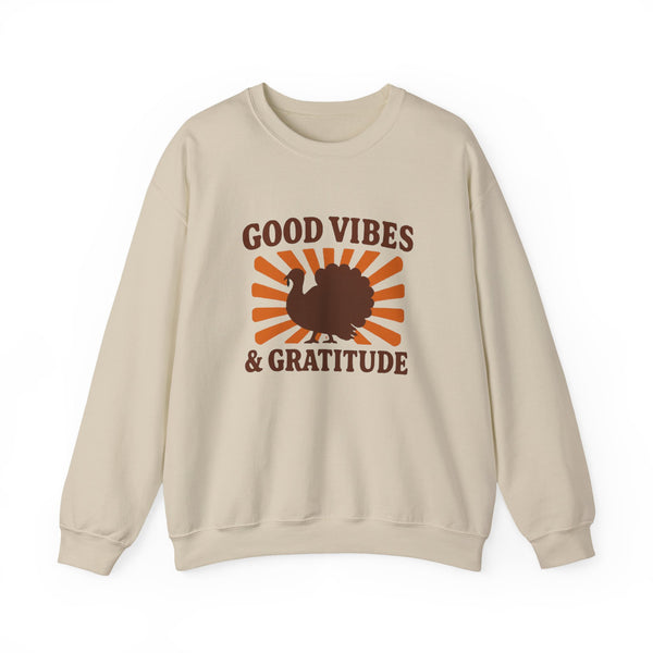 A beige crewneck sweatshirt featuring a 'Good Vibes & Gratitude' graphic with a brown turkey silhouette and orange sunburst rays on the front, displayed against a solid white background.