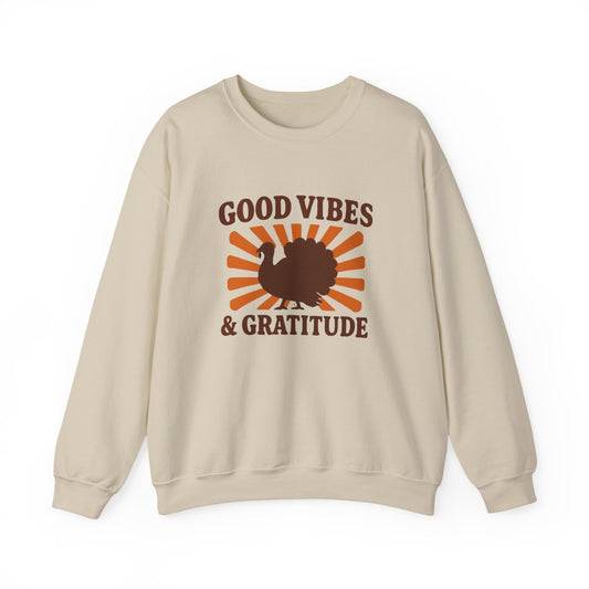 A beige crewneck sweatshirt featuring a 'Good Vibes & Gratitude' graphic with a brown turkey silhouette and orange sunburst rays on the front, displayed against a solid white background.