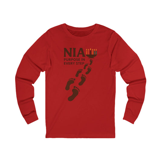 A red long-sleeve t-shirt with a dark brown graphic on the chest featuring the text 'NIA PURPOSE IN EVERY STEP' and footprints leading to a menorah illustration, displayed on a solid white background.