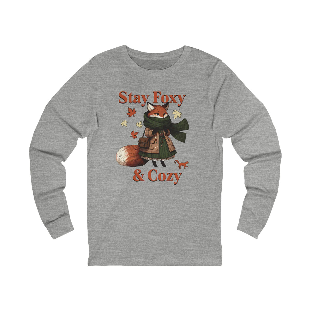 A heather gray long-sleeve t-shirt featuring a cartoon graphic of a cozy fox wearing a green scarf and patterned coat, surrounded by autumn leaves, with the text 'Stay Foxy & Cozy' printed in orange.