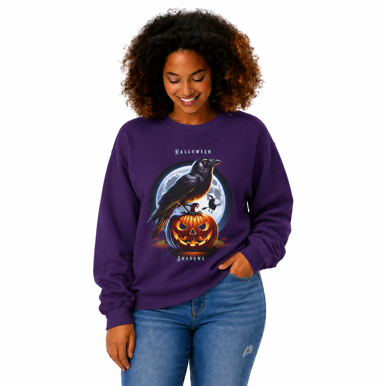 A woman wearing a purple crewneck sweatshirt with a Halloween graphic of a raven on a jack-o'-lantern in front of a full moon, paired with blue jeans, against a plain white background.