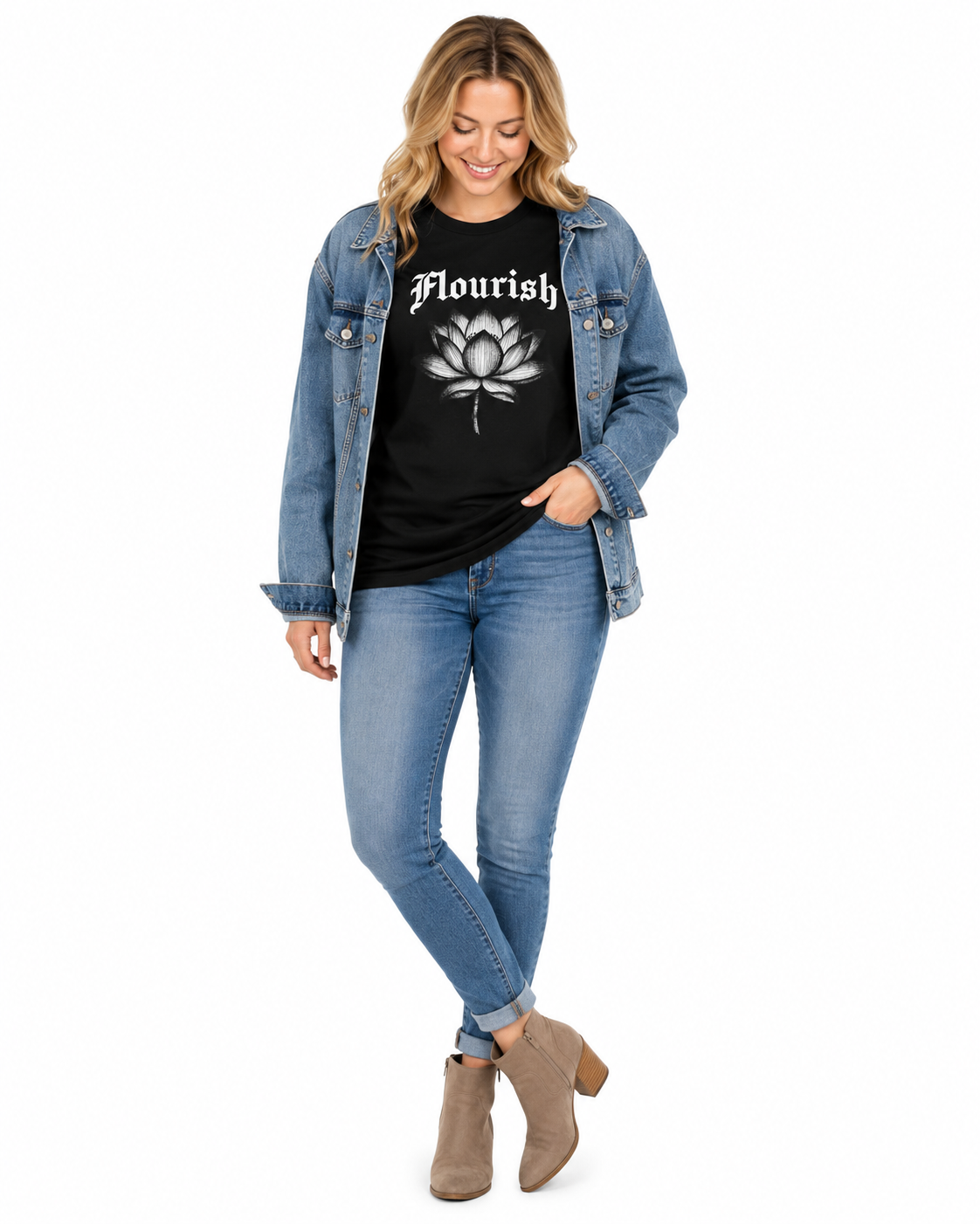 A woman modeling a black graphic t-shirt with a white lotus flower and the word 'Flourish' in a gothic font, styled with a blue denim jacket, blue jeans, and taupe ankle boots against a white background.