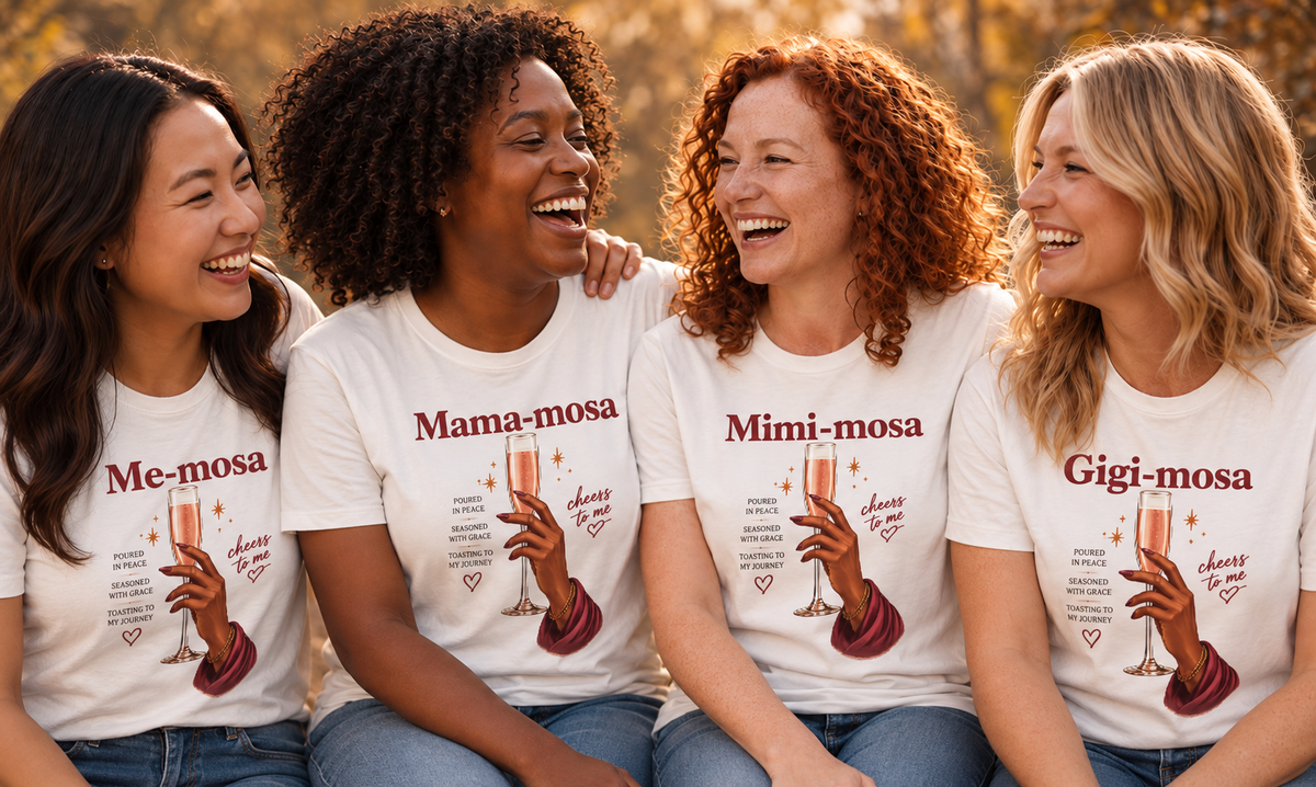 Four women sitting together outdoors wearing matching white graphic T-shirts with the names 'Me-mosa', 'Mama-mosa', 'Mimi-mosa', and 'Gigi-mosa' printed above an illustration of a hand holding a champagne flute.
